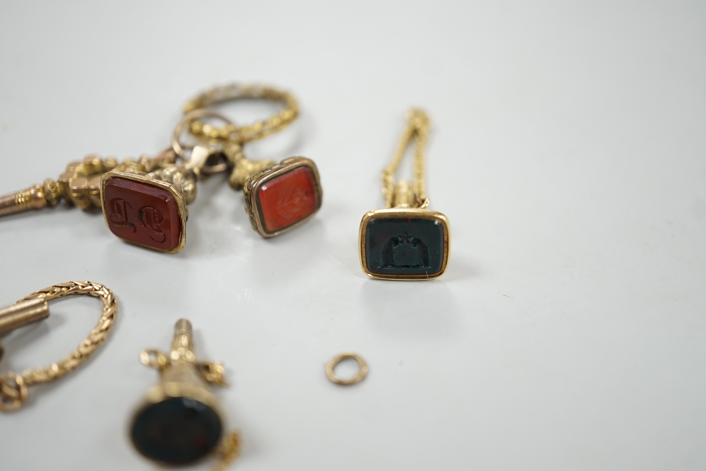 Two 19th century yellow metal overlaid and bloodstone set watch key fobs, one of funnel form, 21mm, a similar gold plated and carnelian set watch key fob, two other fob seals and a watch key on chain.